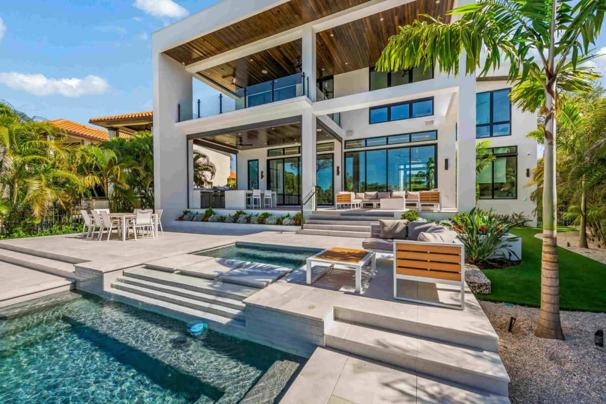 Modern white custom home with covered lanai, pool steps and tropical landscaping