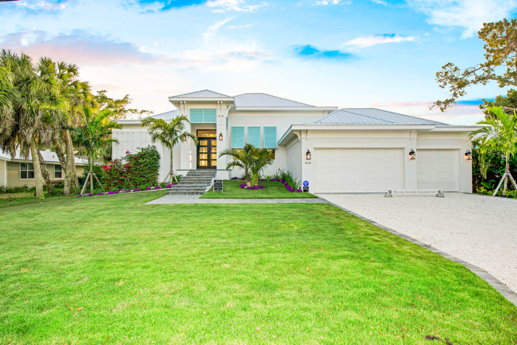 Nutter Custom Construction coastal-style custom home exterior in Sarasota, FL, with metal hip roof, aqua shutters, and three-car garage
