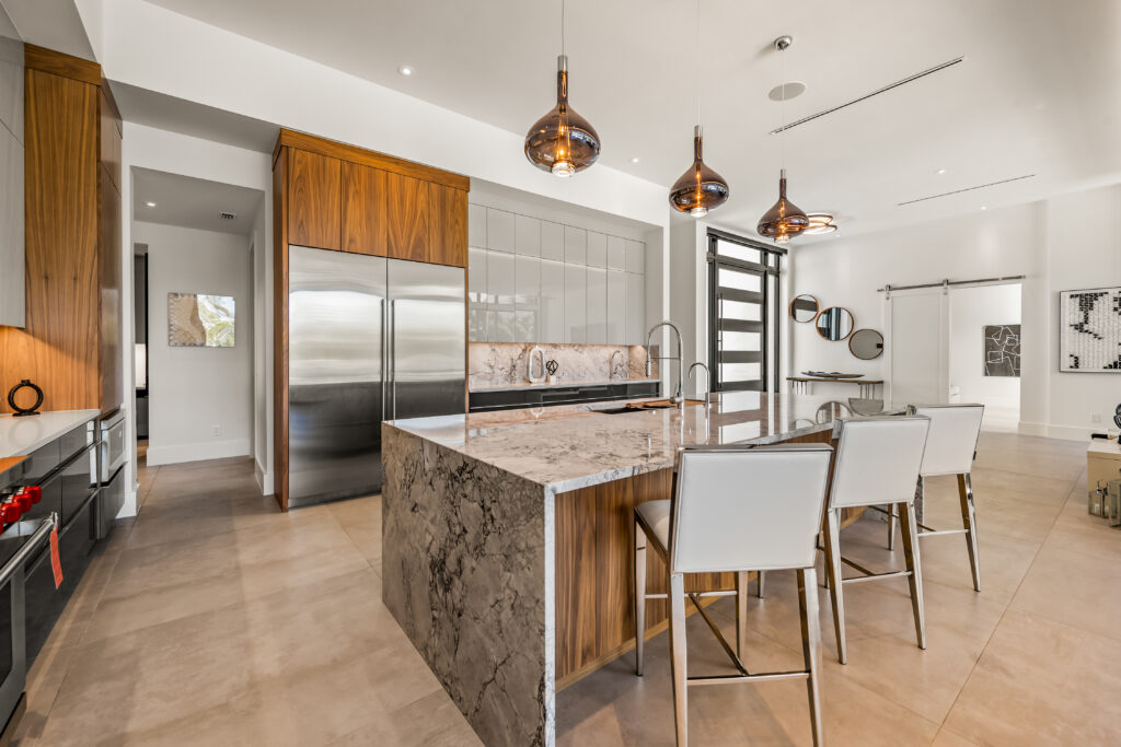 siesta key luxury home contractors Luxury kitchen remodel with marble waterfall island walnut cabinetry and pendant lighting in a Sarasota FL custom home by Nutter Custom Construction