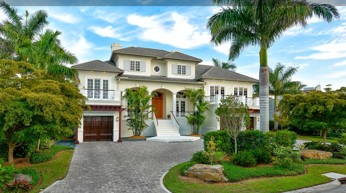 Traditional luxury custom home exterior with arched entry paver driveway and mature palm trees in Sarasota FL built by Nutter Custom Construction